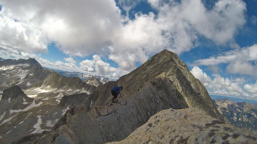 Climber ascending rocky mountain ridge under blue sky with scattered clouds