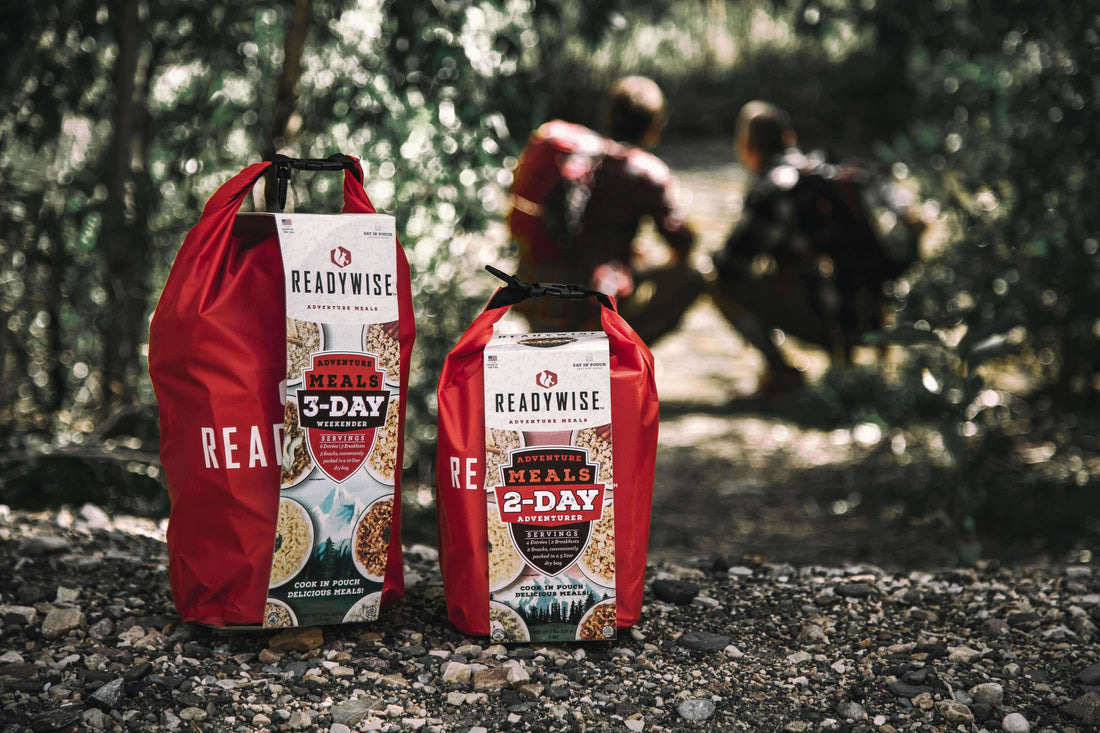 ReadyWise adventure meals 3-day and 2-day kits on forest ground, hikers in background