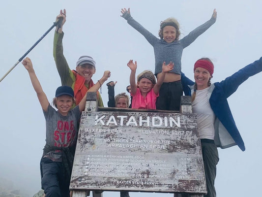 Group of happy hikers celebrating at Mount Katahdin summit sign, Appalachian Trail, foggy day