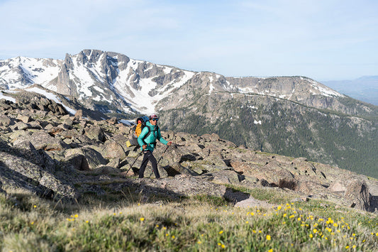 Hiker trekking with backpack on rocky mountain trail, snowy peaks in background