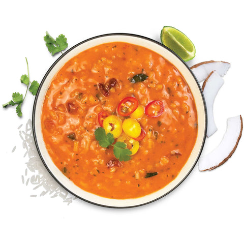 Red Thai curry soup with rice, garnished with peppers, cilantro, lime, coconut, overhead view